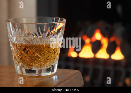 Dram of single malt Scotch whisky in a crystal whiskey glass on a table by an open coal fire England UK Britain Stock Photo