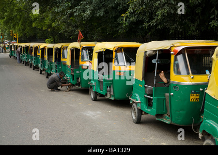 A line of rickshaws waiting for customers. One driver is asleep and another is looking at a wheel. Delhi. India. Stock Photo