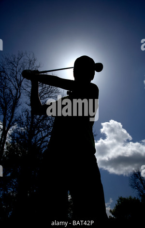silhouette of young golfer holding a golf club driver about to swing to strike the ball against blue cloudy sky Stock Photo