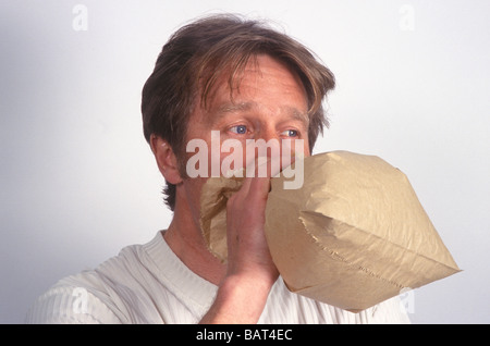 man breathing into a brown paper bag as a remedy for asthma or breathlessness Stock Photo