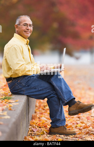 Hispanic man using laptop outdoors in autumn Stock Photo