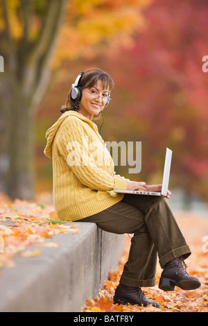 Hispanic woman using laptop outdoors with headphones Stock Photo