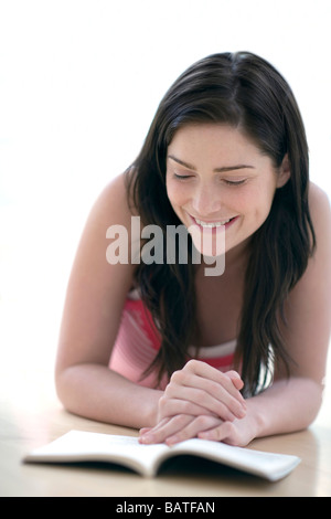 Woman reading while lying on thefloor. She is in her twenties. Stock Photo