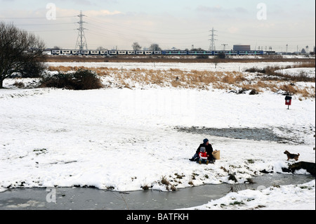 Woman with child sitting in the snow on Walthamstow marshes Lea valley London Stock Photo