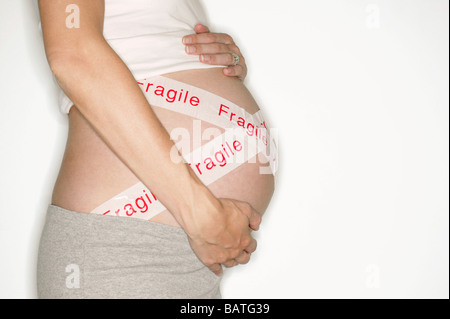 Fragile foetus. Pregnant woman holding her swollen abdomen, which is taped with protective stickers. Stock Photo