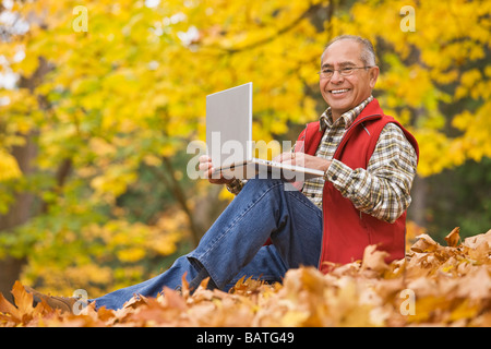 Hispanic man using laptop sitting in autumn leaves Stock Photo