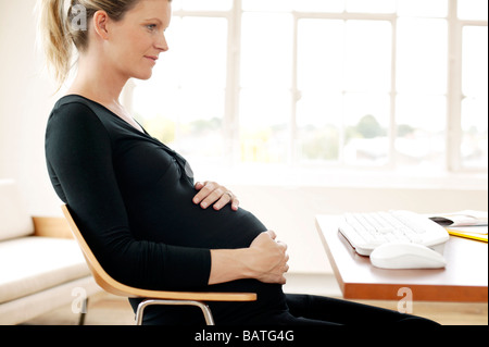 Pregnant woman sitting at her computer desk. She is in her third trimester. Stock Photo