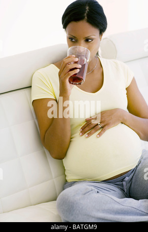 Pregnant woman drinking a glass of cranberry juice. She is at full term. Stock Photo