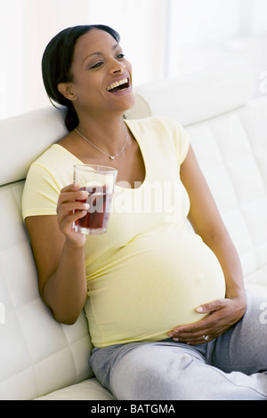 Pregnant woman laughing while holding a glass of cranberry juice. She is at full term. Stock Photo