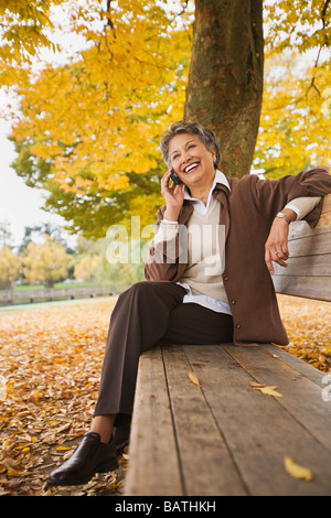 African woman talking on cell phone on park bench in autumn Stock Photo
