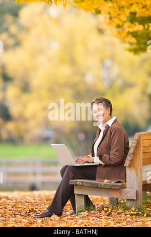 African woman using laptop on park bench in autumn Stock Photo