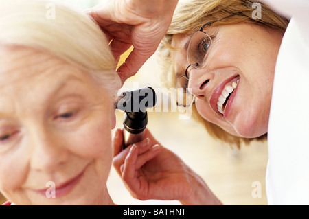 Ear examination. General practice doctor examining a 63-year-old woman's ear using an otoscope. Stock Photo