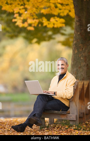 African man using laptop on park bench in autumn Stock Photo