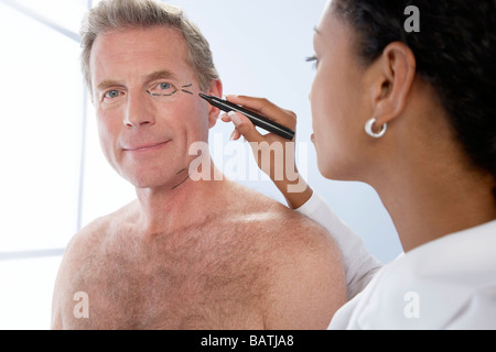 Cosmetic surgery. Cosmetic surgeon making marks on the face of a middle-aged man contemplating cosmetic surgery. Stock Photo