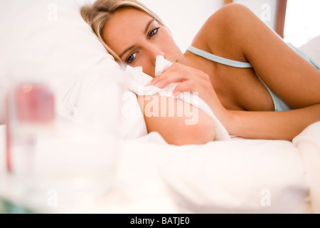 Cold remedies on a bedside table by a woman ill in bed. Stock Photo