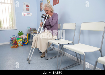 Elderly patient leaning on her crutches in a general practice waiting room. Stock Photo