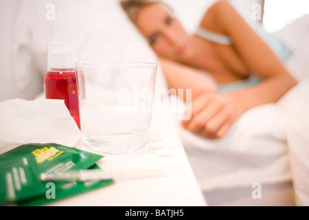 Cold remedies on a bedsidetable by a woman ill in bed. Stock Photo