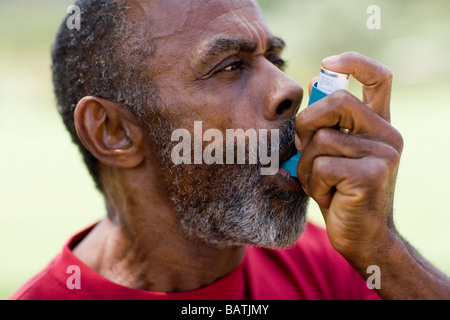 Treating an asthma attack. Elderly man using an inhaler to treat an asthma attack. Stock Photo