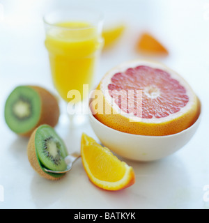 Assorted fruits, including an orange slice, a pink grapefruit (in bowl) and a halved kiwi fruit. Stock Photo