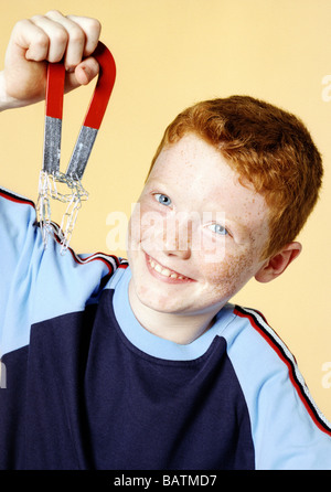 Magnet. Nine year old boy lifting paper clips with a horseshoe magnet. Stock Photo