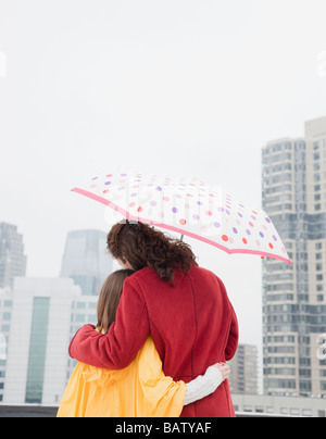 USA, New York City, mother and daughter (10-11 years) embracing under umbrella, rear view