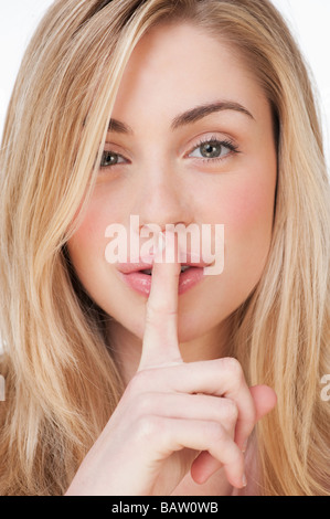Studio portrait of young woman with finger to lips Stock Photo