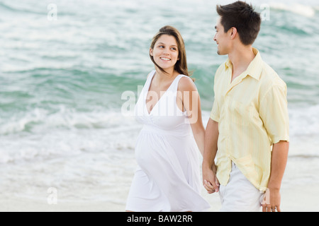 Husband holding hands with pregnant wife on beach Stock Photo