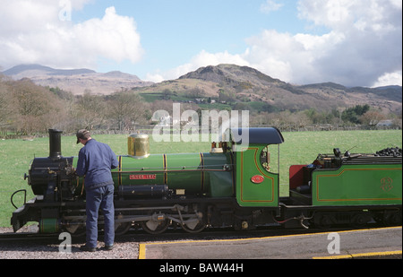 An engineer maintains a 15 inch gauge steam locomotive train before departure with the hills of Eskdale in the background. Stock Photo