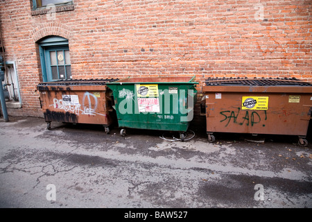 A group of garbage cans containers dumpsters and recycle bins in an alley Stock Photo