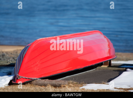 Red fiberglass rowboat  / skiff / dinghy upturned at Winter Stock Photo