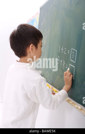 Boy solving mathematical equation on blackboard side view Stock Photo