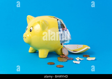 broken yellow piggy bank filled with european currency bills and coins on blue background Stock Photo