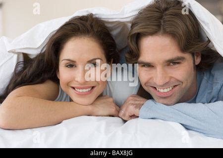 Hispanic couple smiling from under covers on bed Stock Photo
