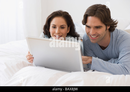 Hispanic couple using laptop on bed Stock Photo