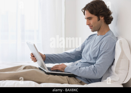 Hispanic man using laptop on bed Stock Photo