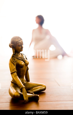 Mid adult woman practising yoga, Buddha figurine in foreground (Half Spinal Twist), yoga studio at Linz, Austria Stock Photo
