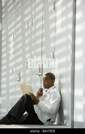 African doctor sitting on floor dictating medical record into recorder Stock Photo