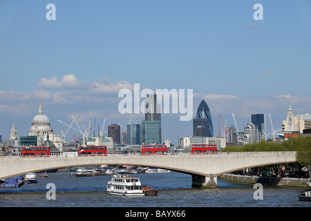 London red buses going over London bridge with the financial district in the background Stock Photo