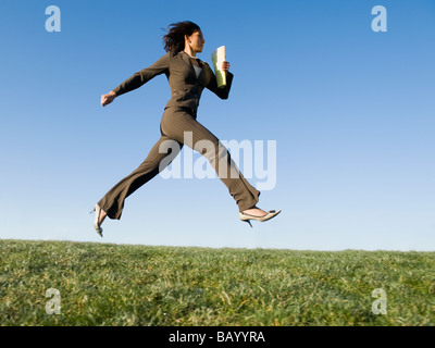 Mixed race businesswoman leaping in field Stock Photo