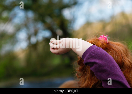 Little girl with red curly hair throwing stones into the river on a sunny day. Stock Photo