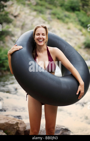 A young caucasian woman in a bikini stands next to a river with a large inner tube. Stock Photo
