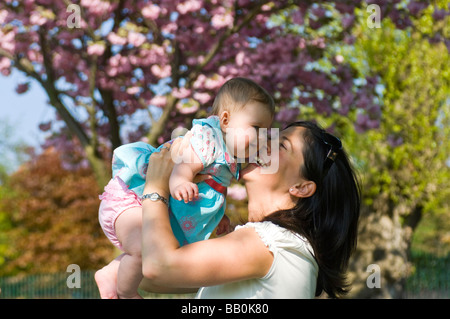 Horizontal close up portrait of a young mum playing with her baby daughter by lifting her up in the air outside in the sunshine Stock Photo