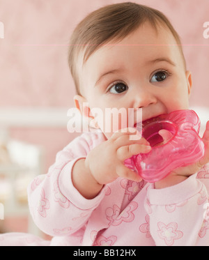 Mixed race baby girl chewing on plastic toy Stock Photo