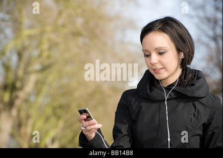 Pretty young teenage girl listening to music on her mp3 player standing outdoors on a spring day Stock Photo