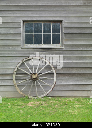 Old wooden cart wheel propped against a barn wall Stock Photo