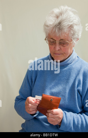 British senior woman wearing a blue jumper taking a ten Euro note from a purse looking concerned. Europe Stock Photo