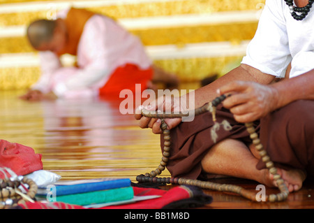 MYANMAR, Yangon. Hands of an asian buddhist man prayingholding a prayer chaplet, a nun in traditional robe praying Stock Photo