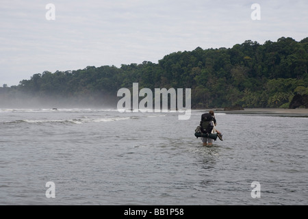 A hiker crosses a river along the coast in Corcovado National Park, Costa Rica. Stock Photo