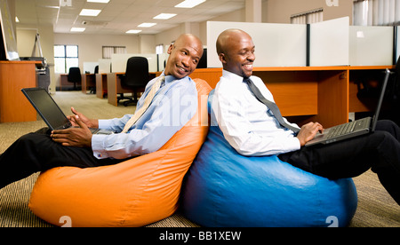 Two businessmen compare work on laptops while sitting on beanbags. Pretoria, South Africa Stock Photo