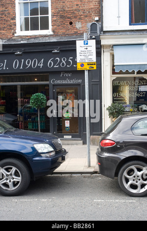Cars parked by a sign showing parking restrictions on city street in England Stock Photo